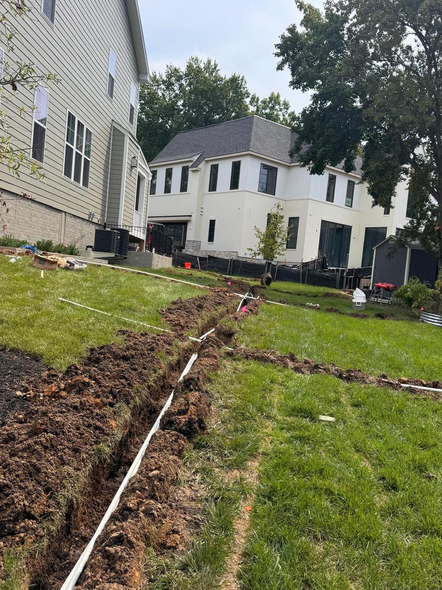Irrigation trench with pipe laid across a backyard lawn between two homes