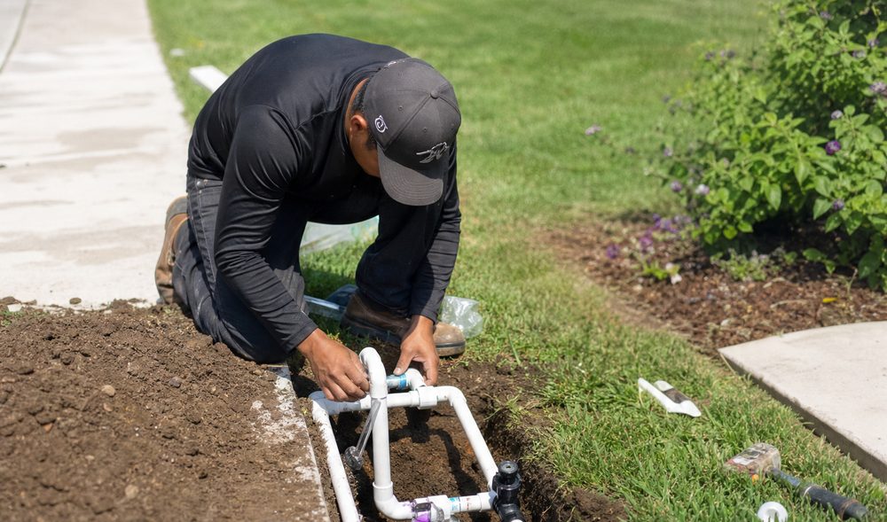 Technician assembling a PVC manifold and valves in an open trench along a sidewalk